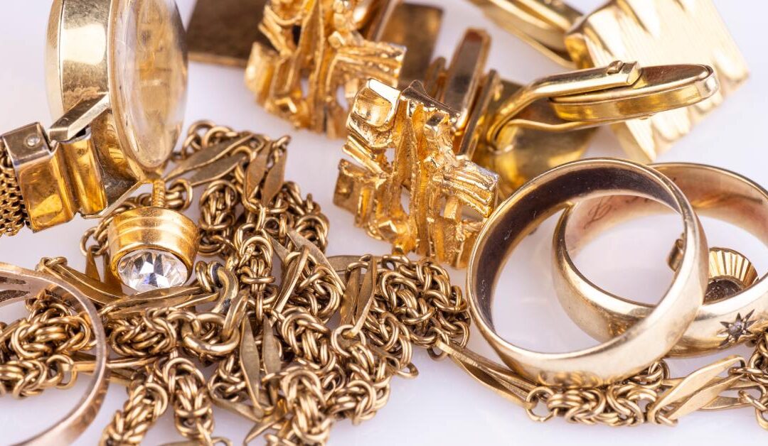 A close-up of multiple gold jewelry including rings, bracelets, watches, and necklaces, piled over a white surface.